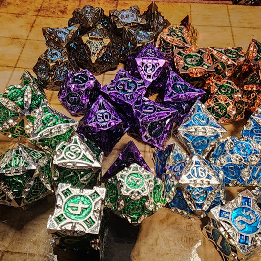 Five finishes of Monuments of the Lost Sands metal dice arranged on a tan grid surface