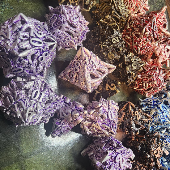 Silver and purple spiky dragon dice alongside brass, copper, red, and blue sets