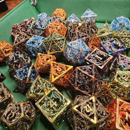 Hollow metal dragon dice in five metallic finishes on a green tray