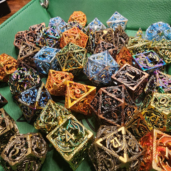 Hollow metal dragon dice in five metallic finishes on a green tray