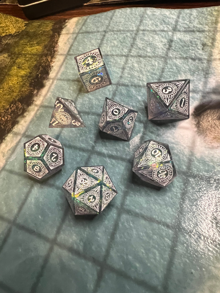 Seven smoky sharp-edge resin dice with colorful inclusions and ornate pale markings