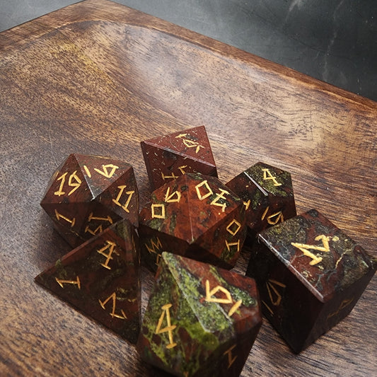 Seven Dragonblood Jasper dice with red-and-green patterns and gold numbering on wood
