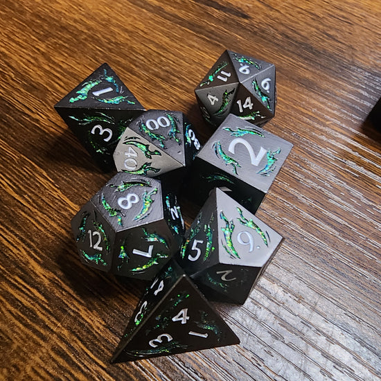 Gunmetal and green seven-piece dagger dice set on a wooden tabletop