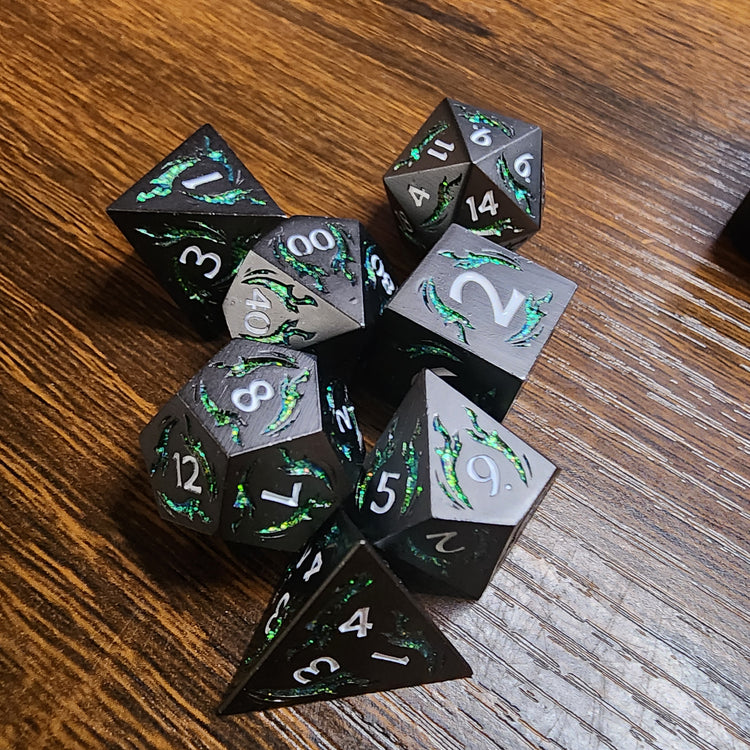 Gunmetal and green seven-piece dagger dice set on a wooden tabletop