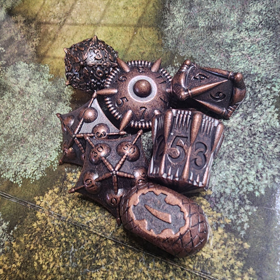 Copper finish seven-piece metal dice set with sculpted artifact shapes and dark recessed details