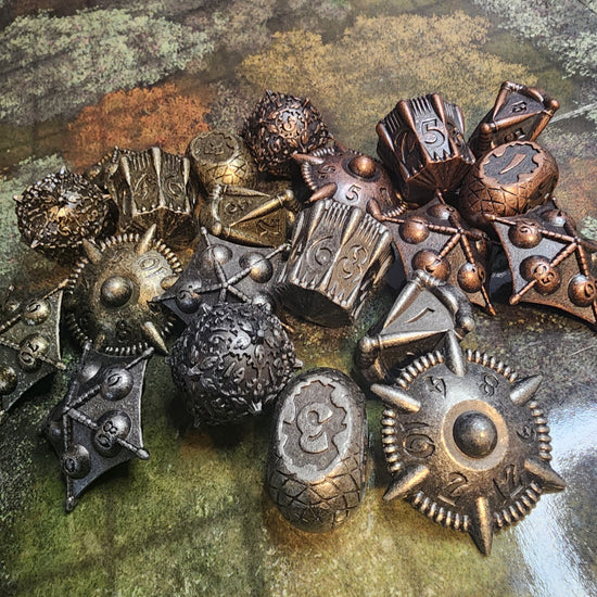Three finishes of seven-piece metal artifact dice arranged on a map-patterned surface