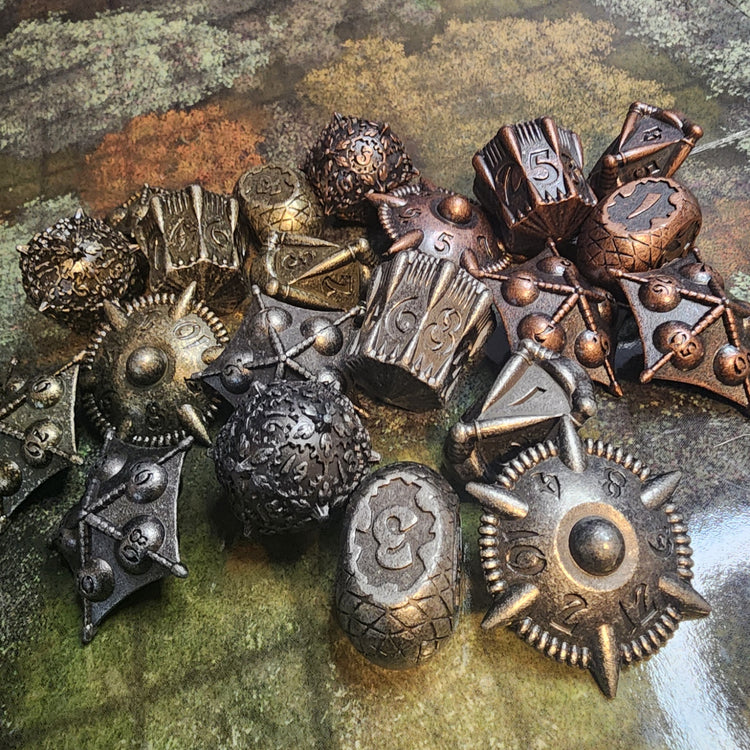 Three finishes of seven-piece metal artifact dice arranged on a map-patterned surface