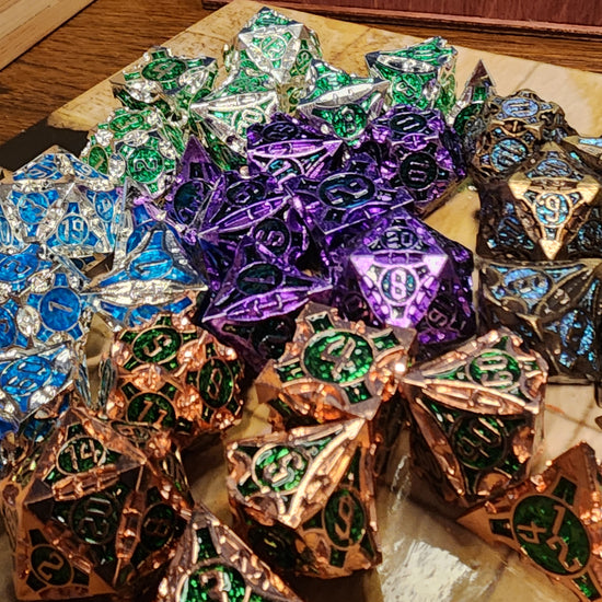 Alternate view of five finishes of Monuments of the Lost Sands metal dice arranged on a tan grid surface