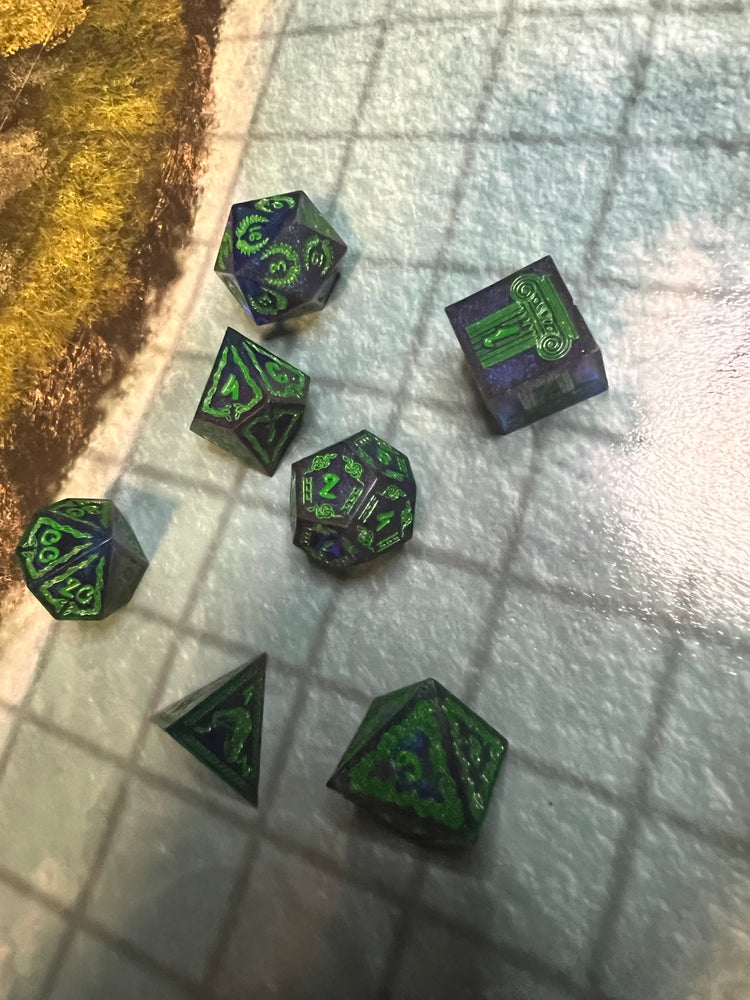 Seven dark blue and purple resin dice with green numbers and snake and column motifs