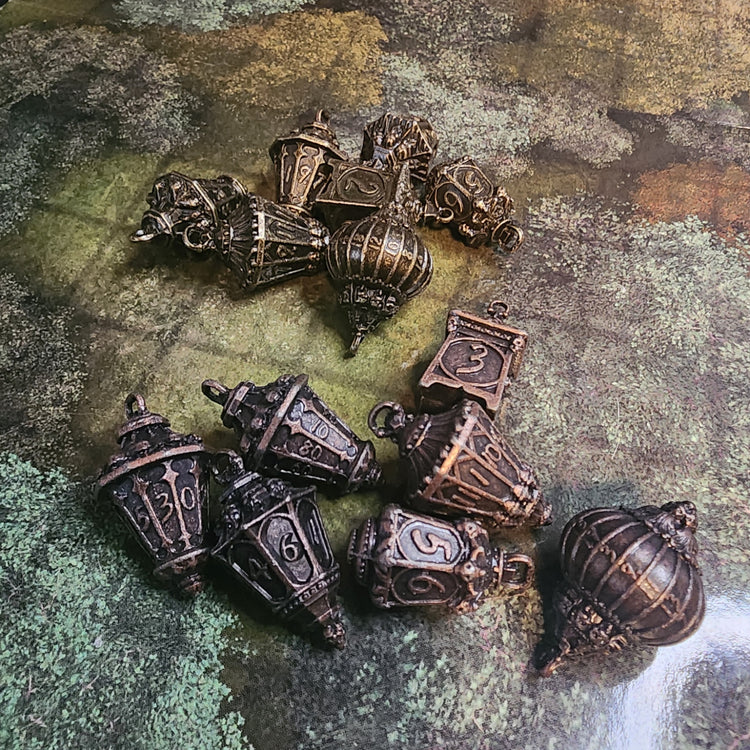 Two forest lantern metal dice sets in brass and copper finishes