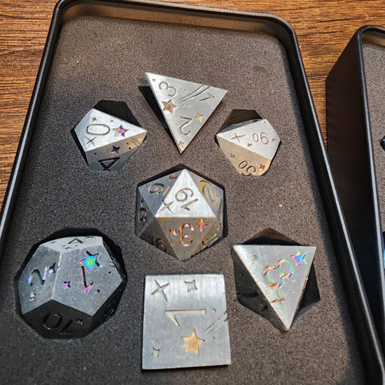 Silver celestial seven-piece metal dice set with rainbow details in its tin