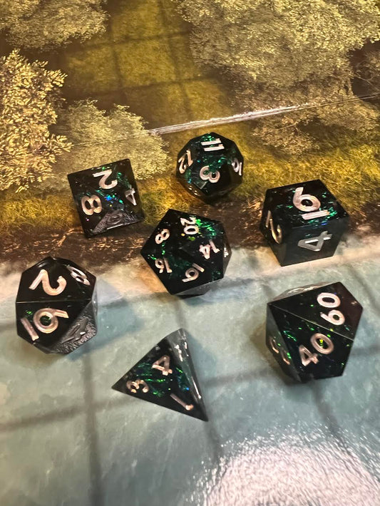 Seven dark sharp-edge resin dice with green shimmer and pale numbers