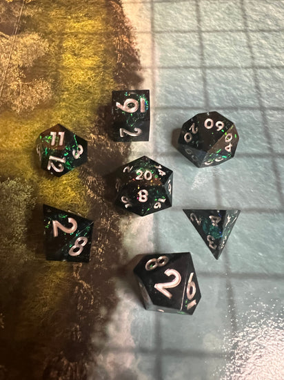 Dark seven-piece resin dice set on a woodland gaming mat